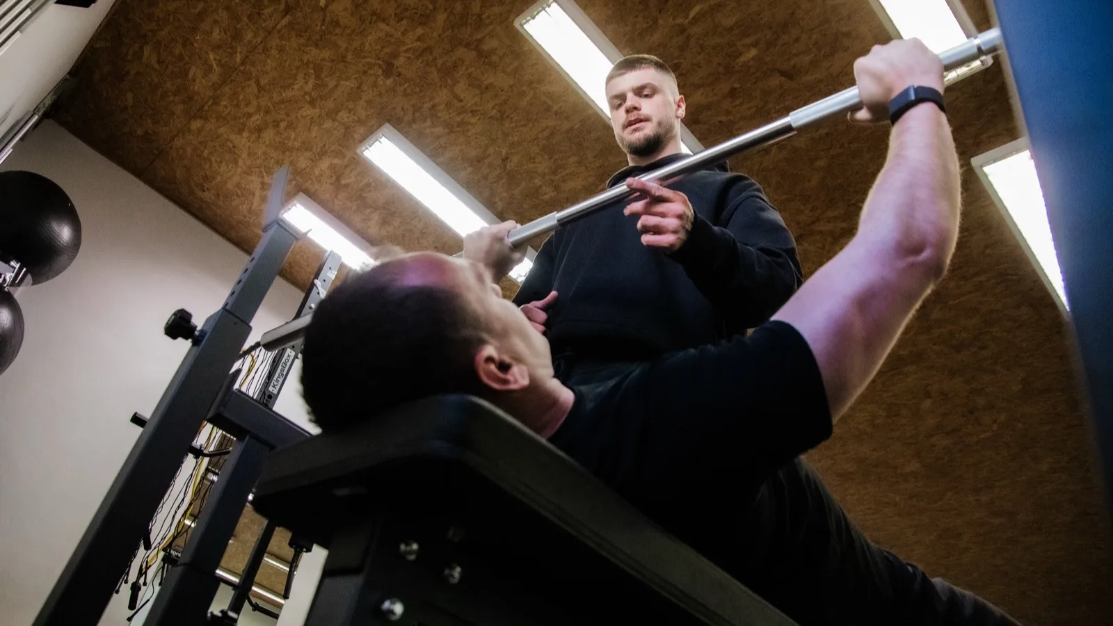 Trenér vede klienta při tlaku na lavici v džimu v Hořovicích