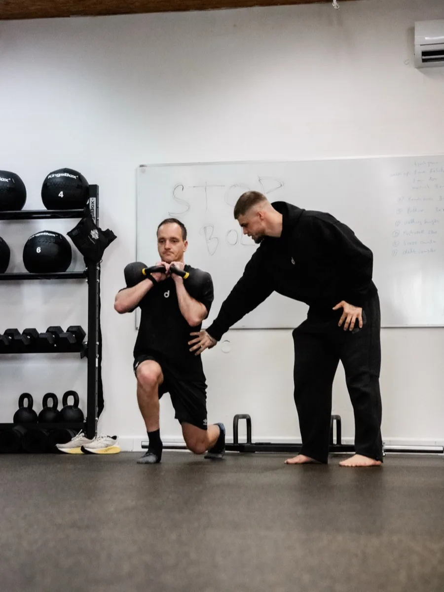Trenér opravuje klientovi provedení výpadu s kettlebellem
